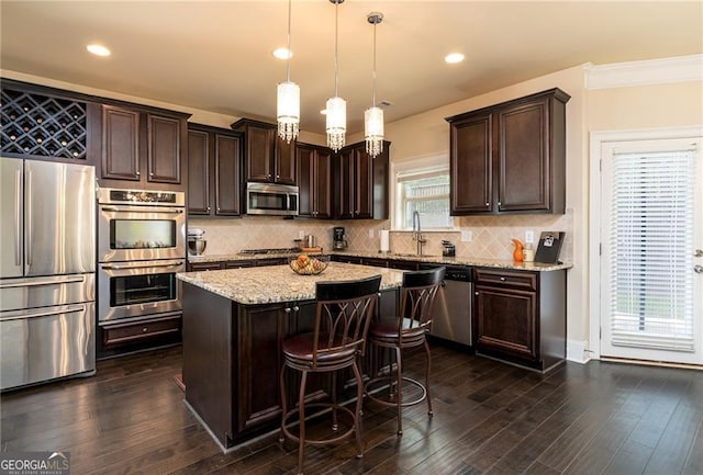 kitchen featuring dark brown cabinetry, backsplash, appliances with stainless steel finishes, a center island, and a sink