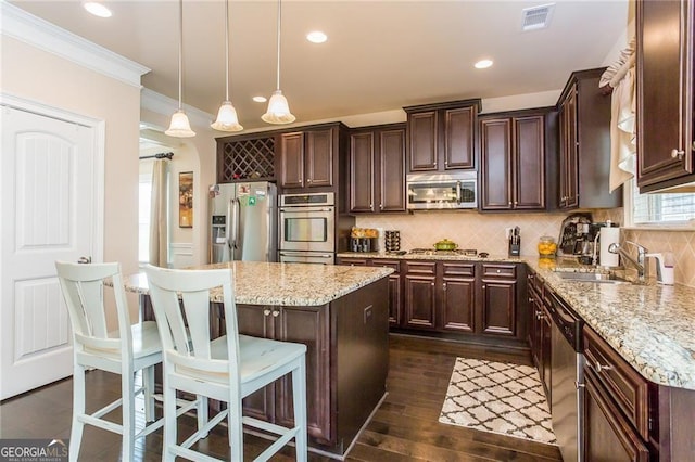 kitchen featuring dark brown cabinetry, appliances with stainless steel finishes, a sink, visible vents, and ornamental molding
