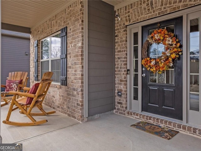 view of exterior entry with a porch and brick siding