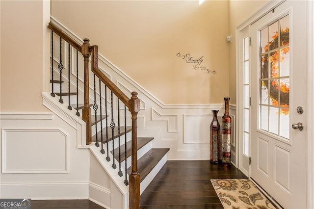 foyer with stairway, a wainscoted wall, a decorative wall, and dark wood-style flooring