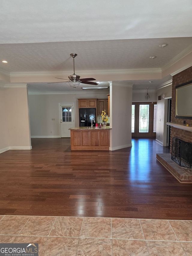 unfurnished living room with dark wood-style flooring, ornamental molding, a ceiling fan, a brick fireplace, and a raised ceiling