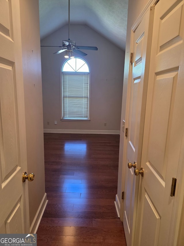 spare room featuring dark wood-type flooring, baseboards, vaulted ceiling, and ceiling fan