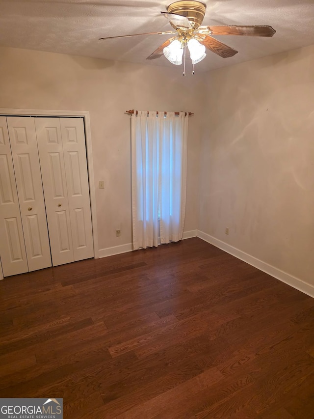 unfurnished bedroom featuring dark wood-type flooring, a closet, ceiling fan, and baseboards