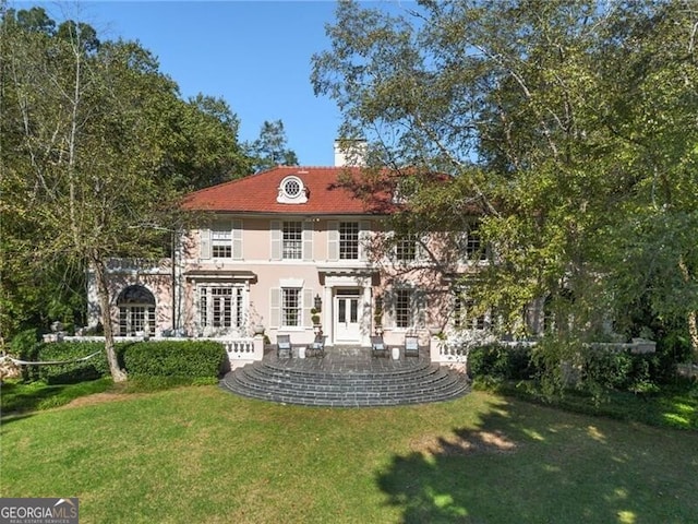 rear view of property with a chimney, a patio area, stucco siding, and a lawn