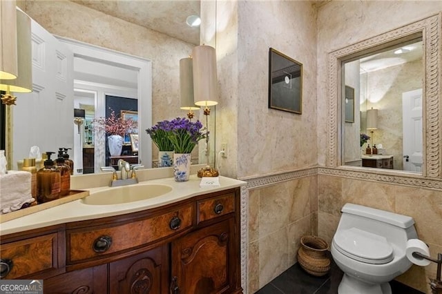 bathroom featuring toilet, vanity, tile patterned flooring, and tile walls