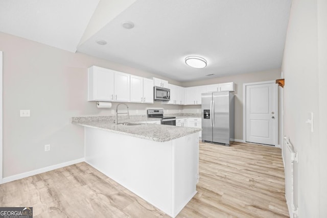 kitchen featuring a peninsula, white cabinetry, appliances with stainless steel finishes, a sink, and baseboards