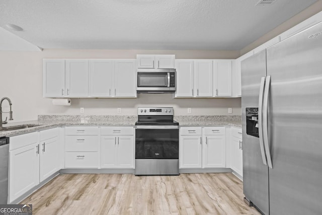kitchen featuring white cabinetry, light stone countertops, appliances with stainless steel finishes, light wood finished floors, and a sink