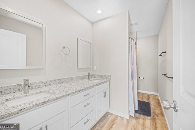 bathroom with double vanity, baseboards, a sink, and wood finished floors