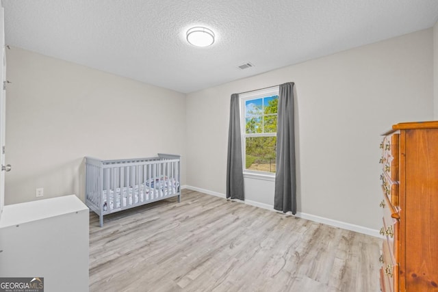 unfurnished bedroom with a textured ceiling, wood finished floors, baseboards, and visible vents