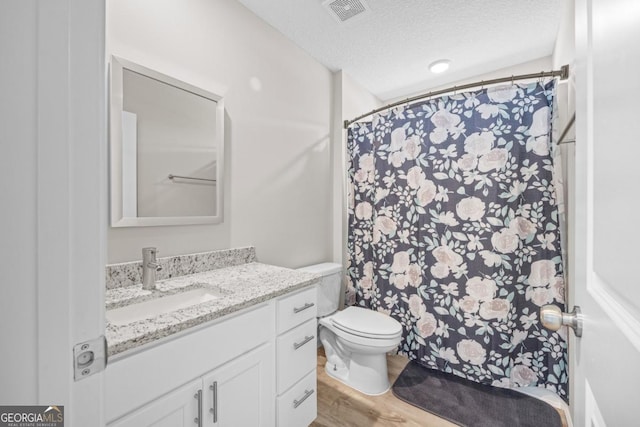 full bath with a textured ceiling, vanity, visible vents, toilet, and wood finished floors