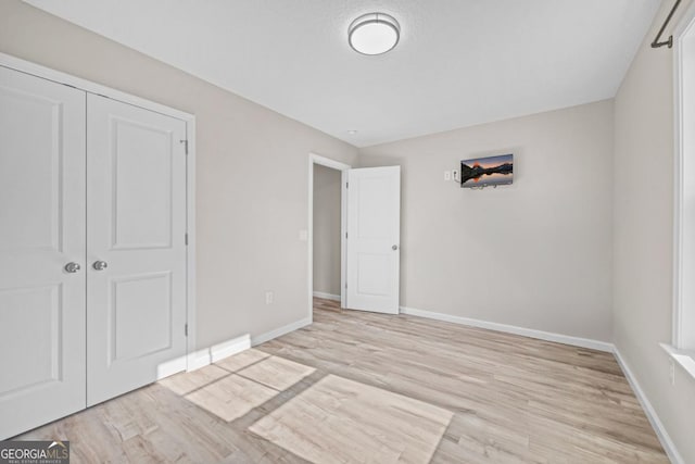 unfurnished bedroom featuring a closet, light wood-style floors, and baseboards