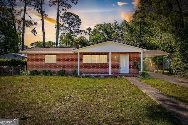 view of front facade with a yard, fence, brick siding, and an attached carport