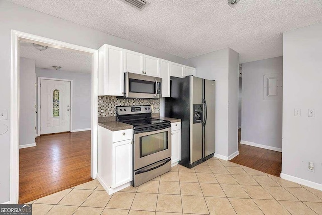 kitchen featuring a textured ceiling, dark countertops, white cabinets, decorative backsplash, and stainless steel appliances