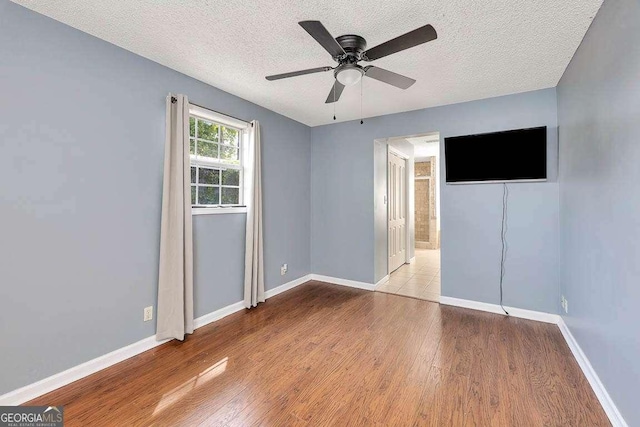 unfurnished bedroom with a textured ceiling, wood finished floors, and baseboards