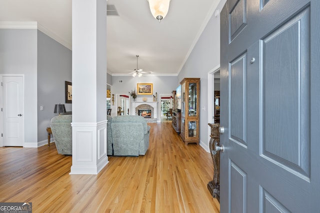 entryway with light wood-type flooring, ornamental molding, and a warm lit fireplace