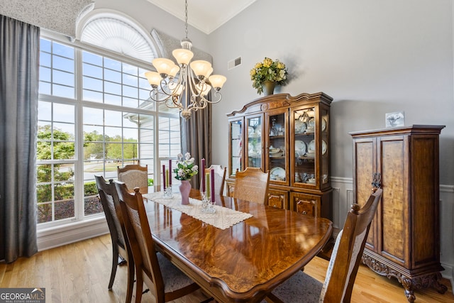 dining area with a notable chandelier, light wood finished floors, visible vents, and ornamental molding
