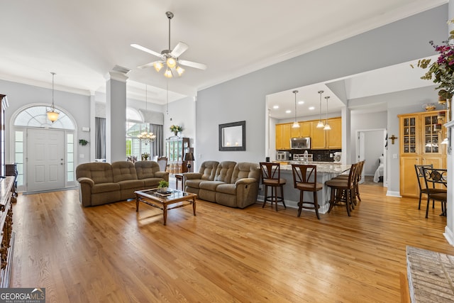 living room featuring light wood finished floors, visible vents, ceiling fan with notable chandelier, and ornamental molding