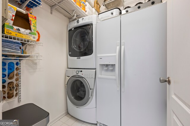 clothes washing area with stacked washer / drying machine, light tile patterned floors, baseboards, and laundry area