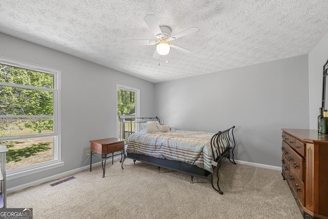 bedroom featuring light carpet, baseboards, visible vents, and a textured ceiling