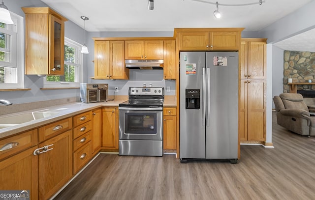 kitchen with light wood-style floors, glass insert cabinets, stainless steel appliances, light countertops, and under cabinet range hood