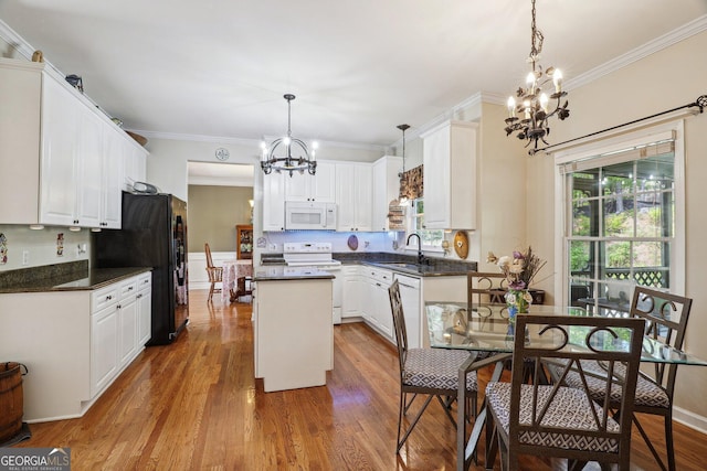 kitchen with dark countertops, a center island, a sink, white appliances, and an inviting chandelier