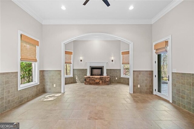 411 River Bluff Ln, Ball Ground, GA 30107 - unfurnished living room with arched walkways, a fireplace with raised hearth, tile walls, ceiling fan, and crown molding