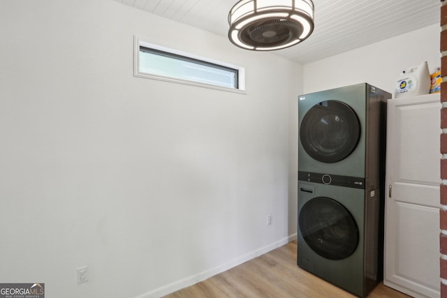 laundry room featuring stacked washer / drying machine, light wood-style flooring, and baseboards