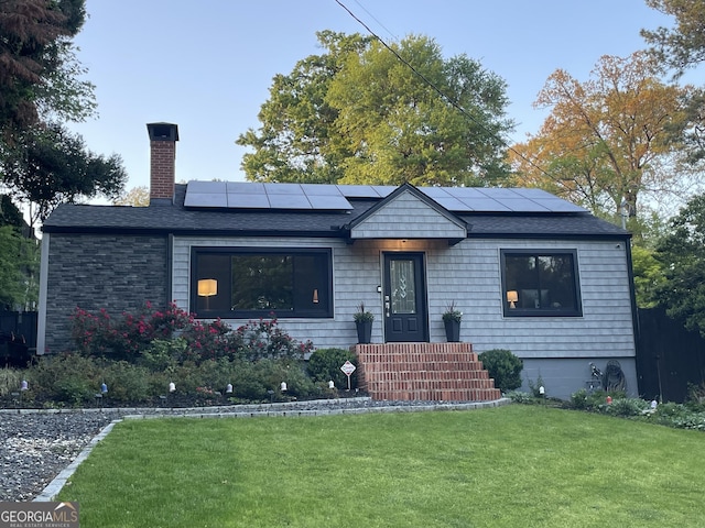 view of front of property featuring a front lawn, a chimney, roof mounted solar panels, and a shingled roof