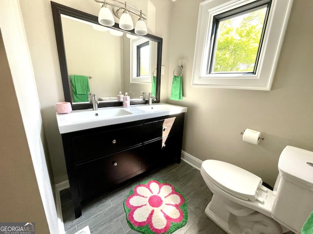 bathroom with toilet, double vanity, and baseboards