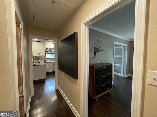 hallway with attic access, dark wood-type flooring, ornamental molding, and baseboards