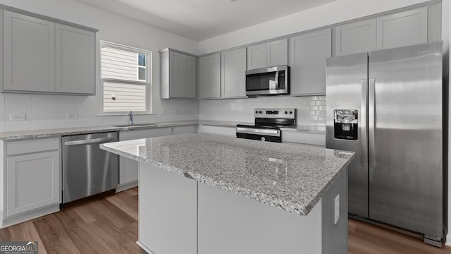 kitchen with dark wood-type flooring, gray cabinets, appliances with stainless steel finishes, a sink, and backsplash