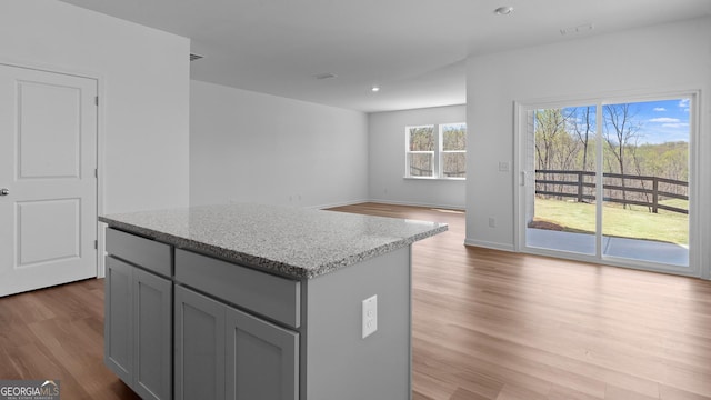 kitchen featuring light wood-style flooring, a kitchen island, gray cabinetry, and light stone counters