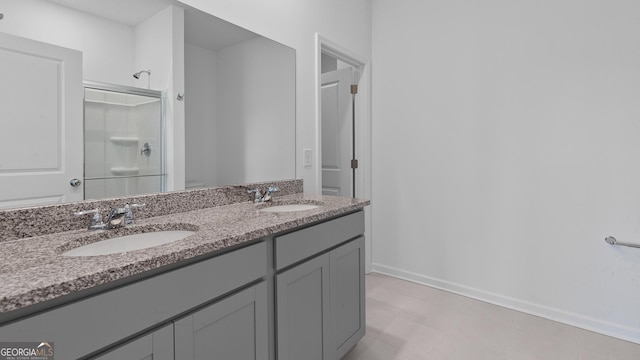 full bathroom with baseboards, double vanity, a sink, and a shower with door