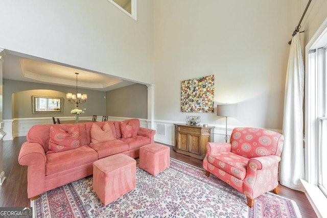 living area featuring wood finished floors, a wainscoted wall, a notable chandelier, a tray ceiling, and ornate columns
