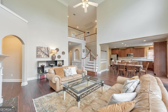 living room with a ceiling fan, arched walkways, baseboards, dark wood-style floors, and a high ceiling