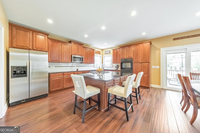 kitchen featuring a kitchen breakfast bar, a kitchen island, backsplash, appliances with stainless steel finishes, and wood finished floors