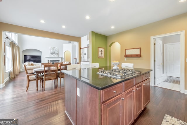 kitchen with stainless steel gas cooktop, a kitchen island, dark wood-type flooring, dark stone counters, and arched walkways
