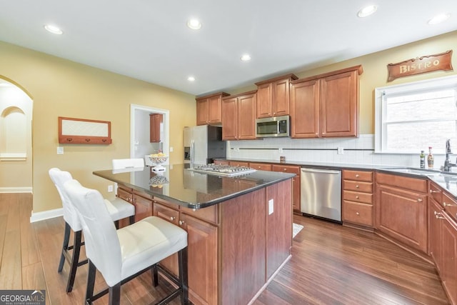 kitchen featuring a breakfast bar, dark wood-style floors, a center island, a sink, and stainless steel appliances