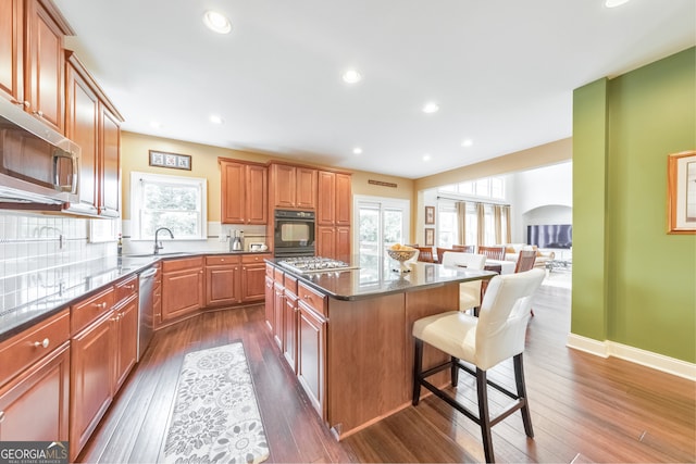 kitchen featuring a kitchen island, a kitchen bar, appliances with stainless steel finishes, arched walkways, and a sink