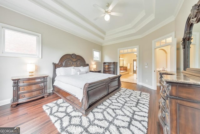 bedroom featuring baseboards, dark wood-style floors, ornamental molding, a tray ceiling, and ensuite bath