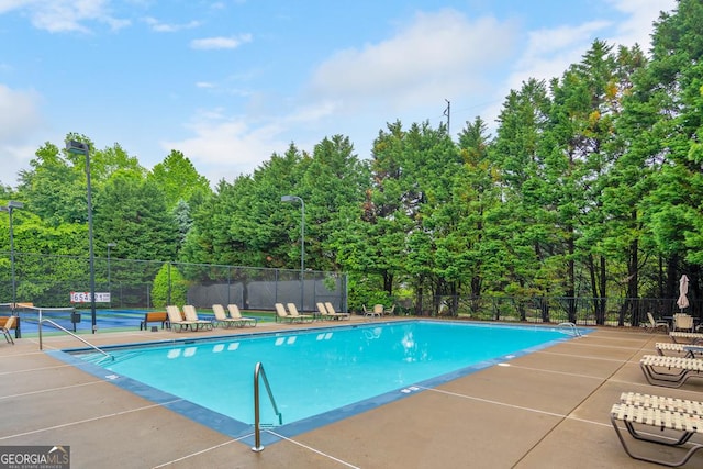 pool with a patio, a tennis court, and fence