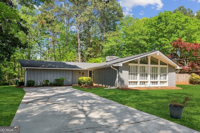 view of front of home with fence, a front lawn, brick siding, a chimney, and driveway