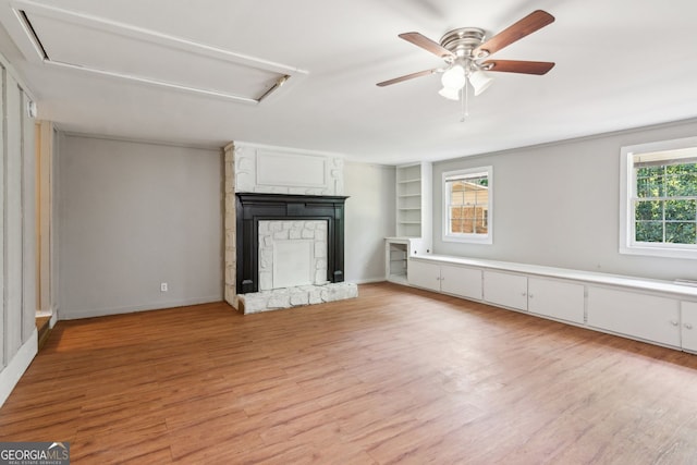 unfurnished living room with built in features, a ceiling fan, attic access, and light wood-type flooring