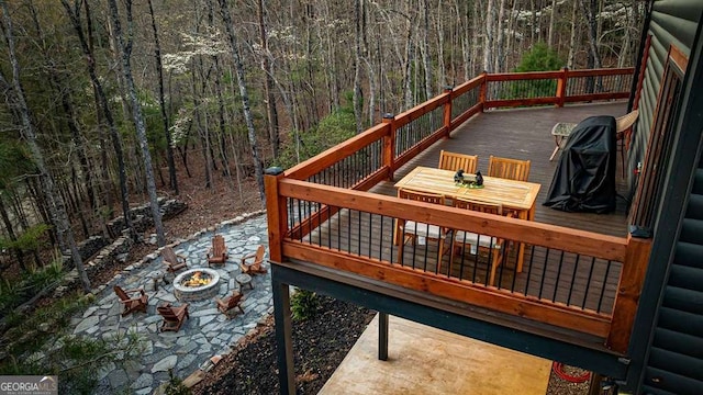 deck featuring an outdoor fire pit, outdoor dining space, and a forest view