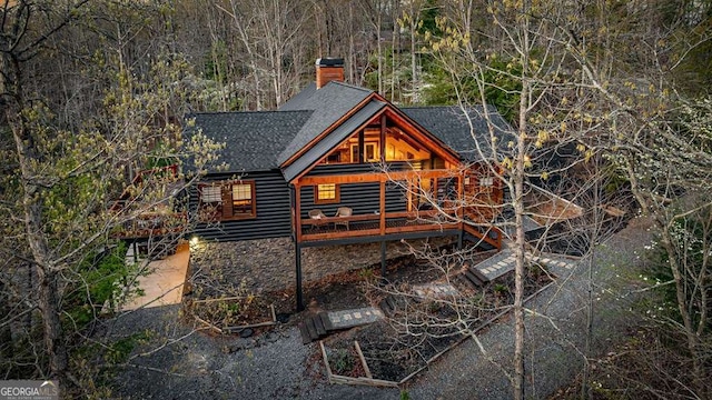 rear view of house featuring roof with shingles, a chimney, and faux log siding
