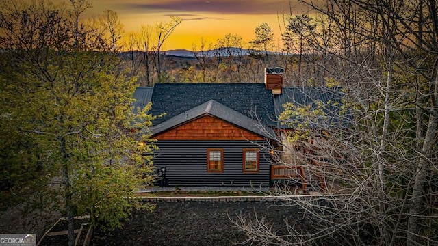 property exterior at dusk with a mountain view, roof with shingles, a chimney, and faux log siding