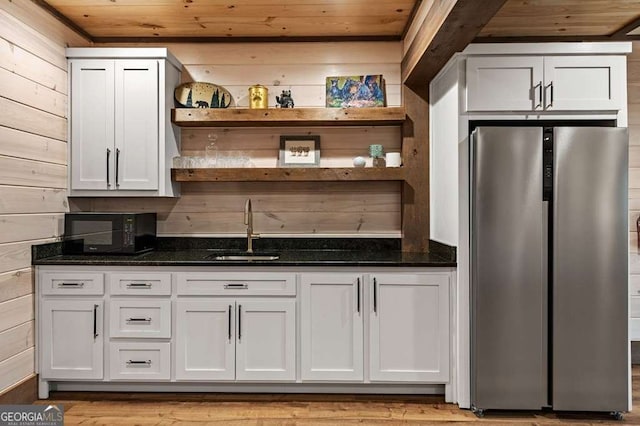 bar with a sink, wood walls, freestanding refrigerator, and wooden ceiling