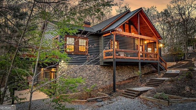 back of house at dusk with a chimney, log veneer siding, stone siding, and stairway