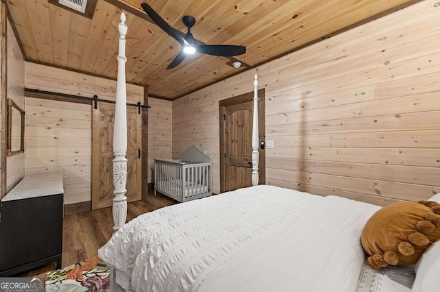 bedroom with wood finished floors, wood walls, wooden ceiling, and a barn door