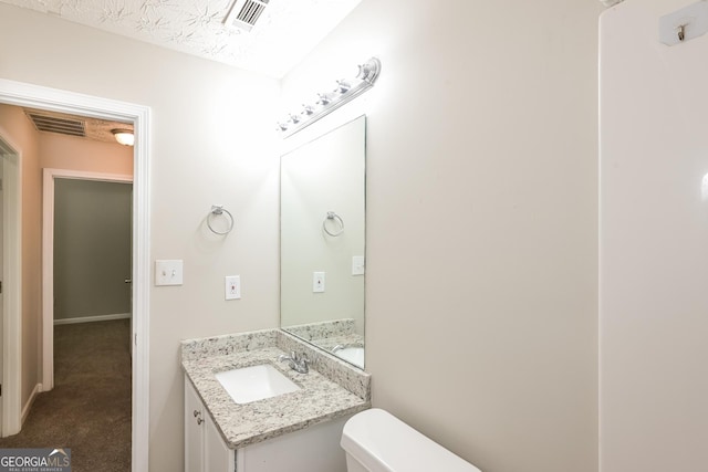 bathroom with toilet, vanity, and visible vents